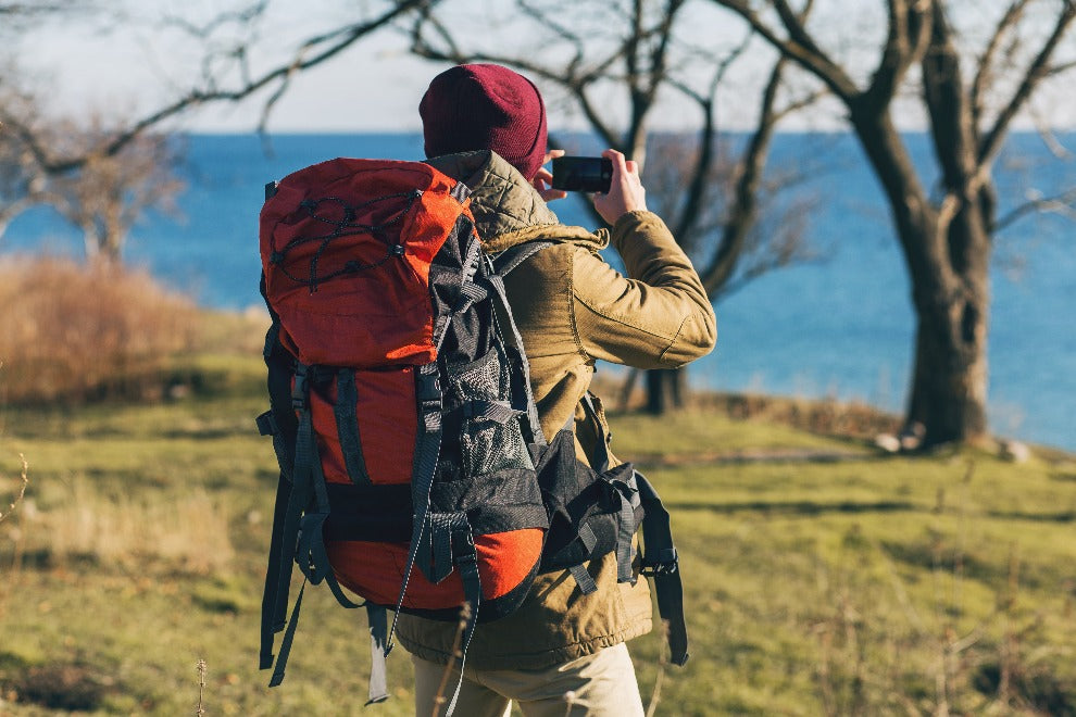 hombre-joven-inconformista-que-viaja-mochila-chaqueta-sombrero-turista-activo-tomando-fotografias-telefono-movil-explorando-naturaleza-estacion-fria.jpg